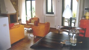 Un coin repas comprenant une table, des chaises et une lampe. Il y a une fenêtre avec des rideaux et une vue sur l’extérieur.