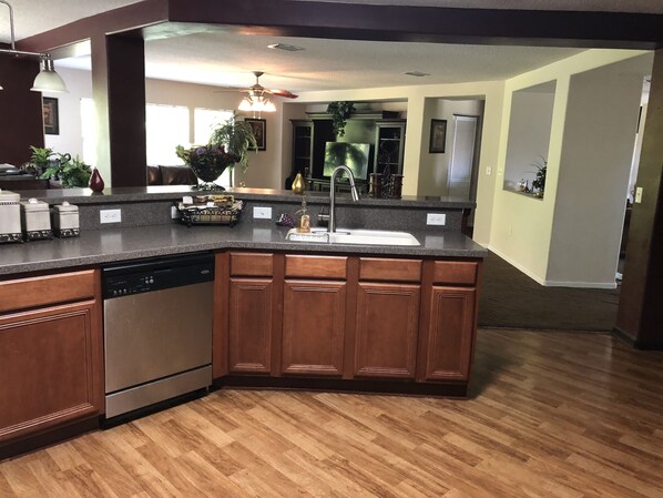 A kitchen with a granite countertop, wooden cabinets, a dishwasher, and a large island with a sink.