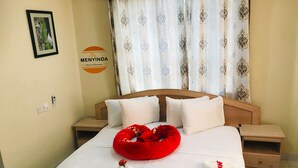 Ein Hotelzimmer mit Bett, weißer Bettwäsche, einem roten Zierkissen und einer Schwan-Handtuch-Arrangement.