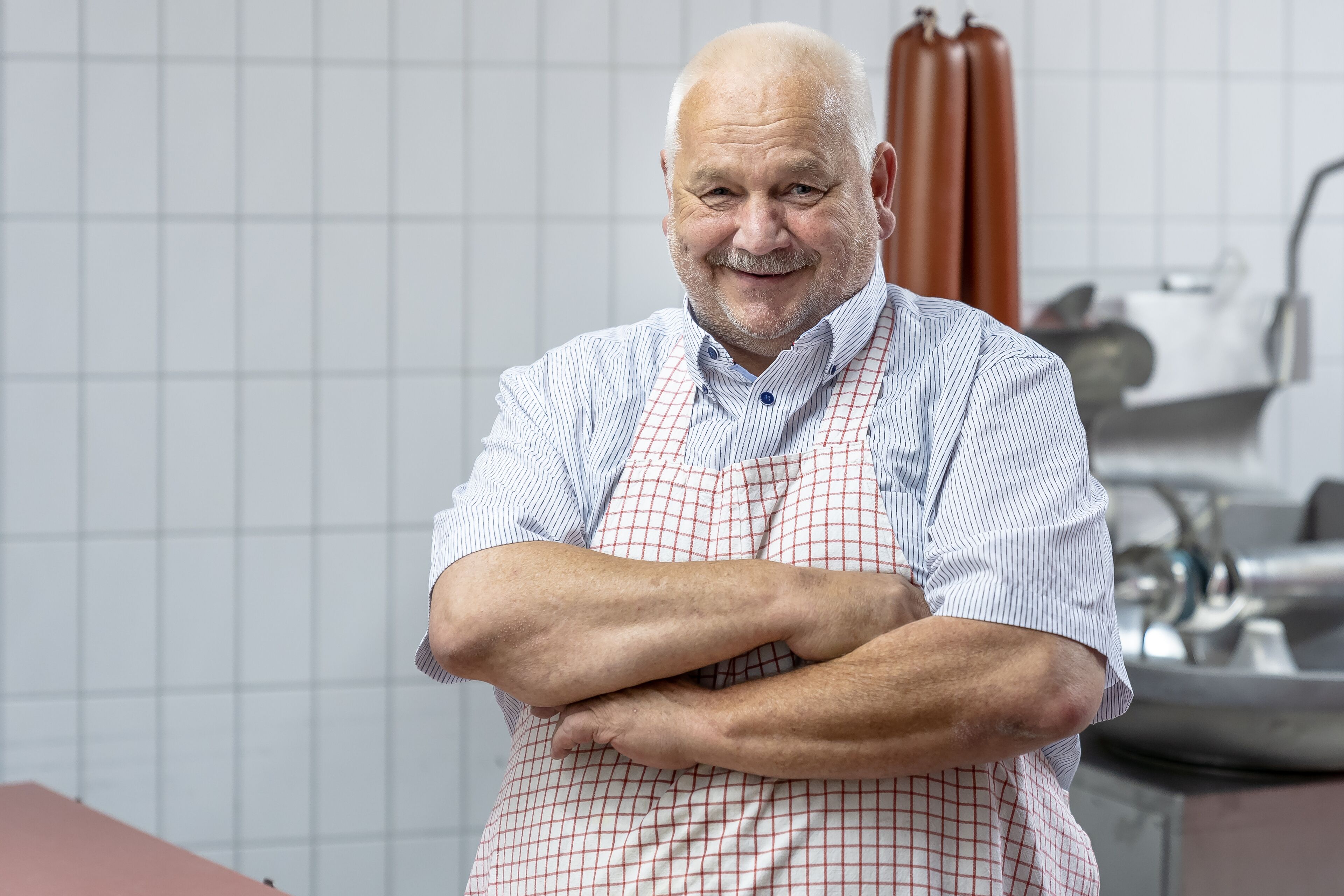 A person standing in a kitchen with crossed arms, wearing a checkered apron.
