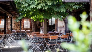 An outdoor dining area with wooden tables and metal chairs, surrounded by trees and brick walls. - Hotel Gasthof Rössle (Weingarten)