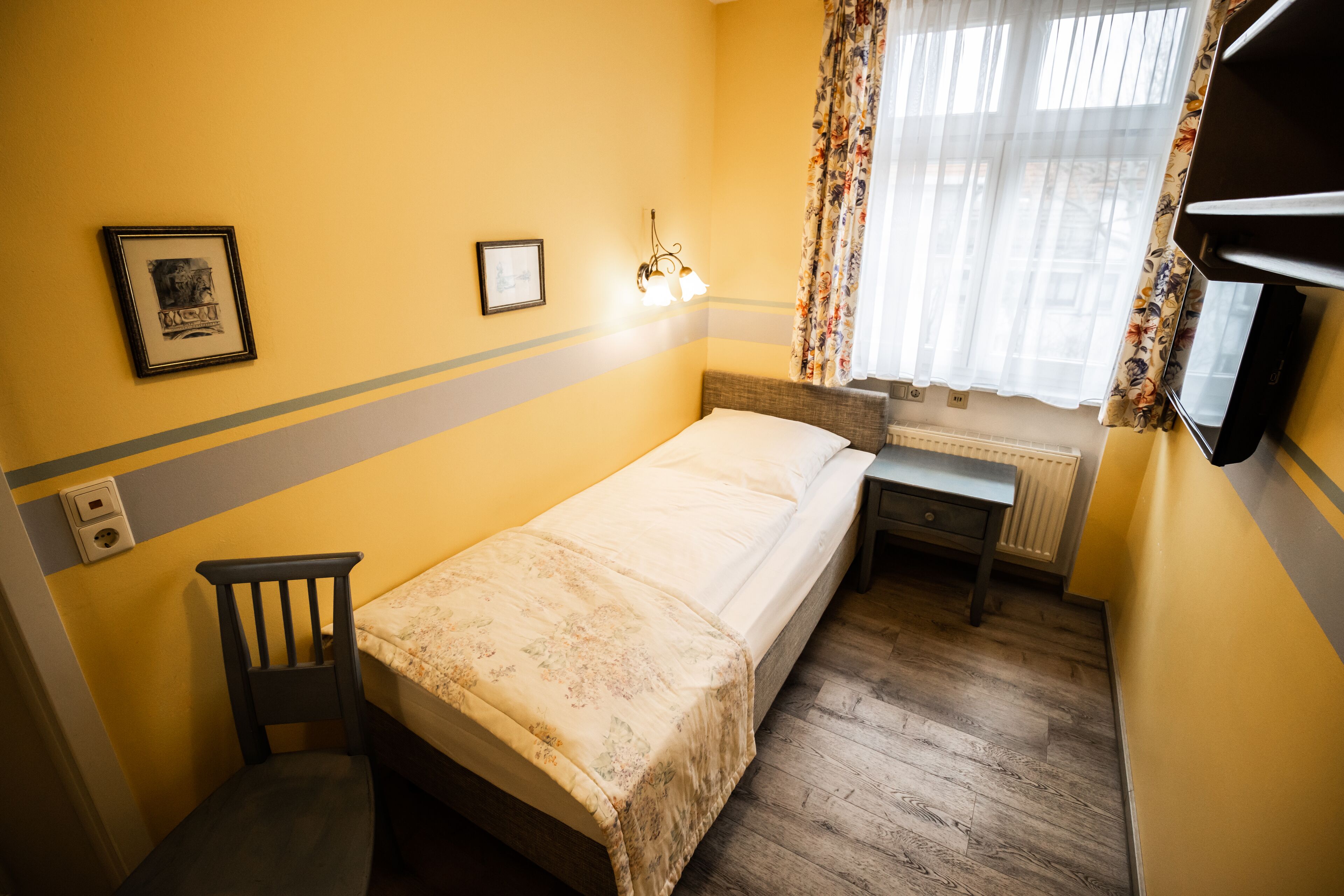 A small, yellow-walled room with a single bed, a chair, a desk, and a radiator.