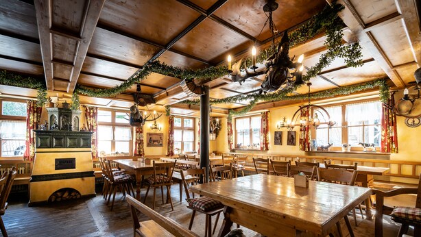 A rustic dining area with wooden tables and benches, a central fireplace, and decorative greenery. - Hotel Gasthof Rössle (Weingarten)