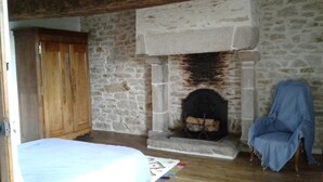 A room with a stone fireplace, a wooden wardrobe, and a bed. - 17th century house in the heart of a charming little village. (Saint-Servant)