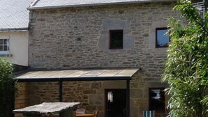 A stone house with a tiled roof, a covered patio, and a small garden area. - 17th century house in the heart of a charming little village. (Saint-Servant)