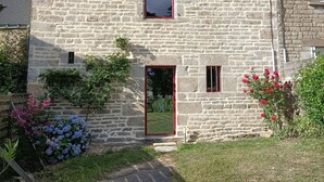 A stone building with a red door, small windows, and a garden with flowers. - 17th century house in the heart of a charming little village. (Saint-Servant)