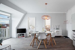 Uma sala de estar moderna com área de jantar, televisão e uma grande janela com vista para o exterior.