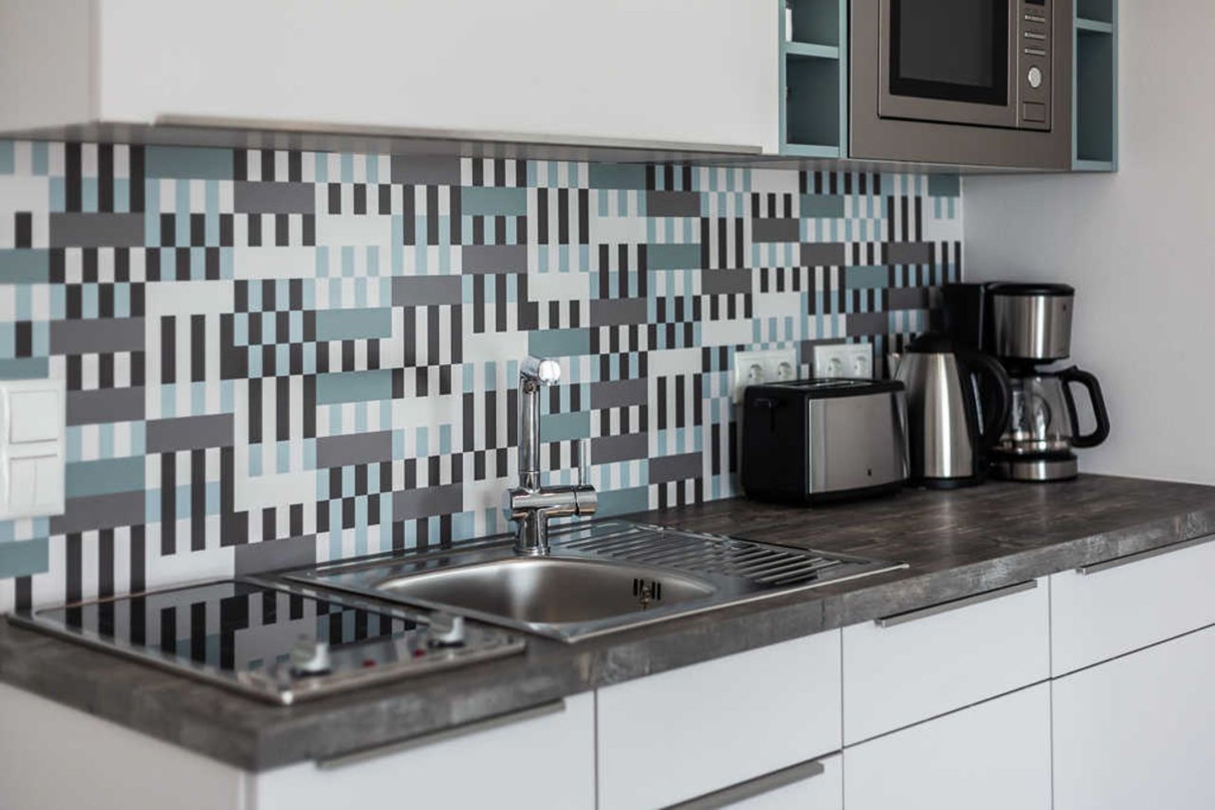 A modern kitchen with a tiled backsplash, stainless steel sink, and a coffee maker.