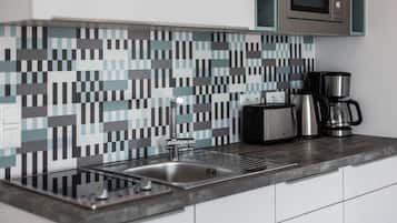A modern kitchen with a tiled backsplash, stainless steel sink, and a coffee maker.
