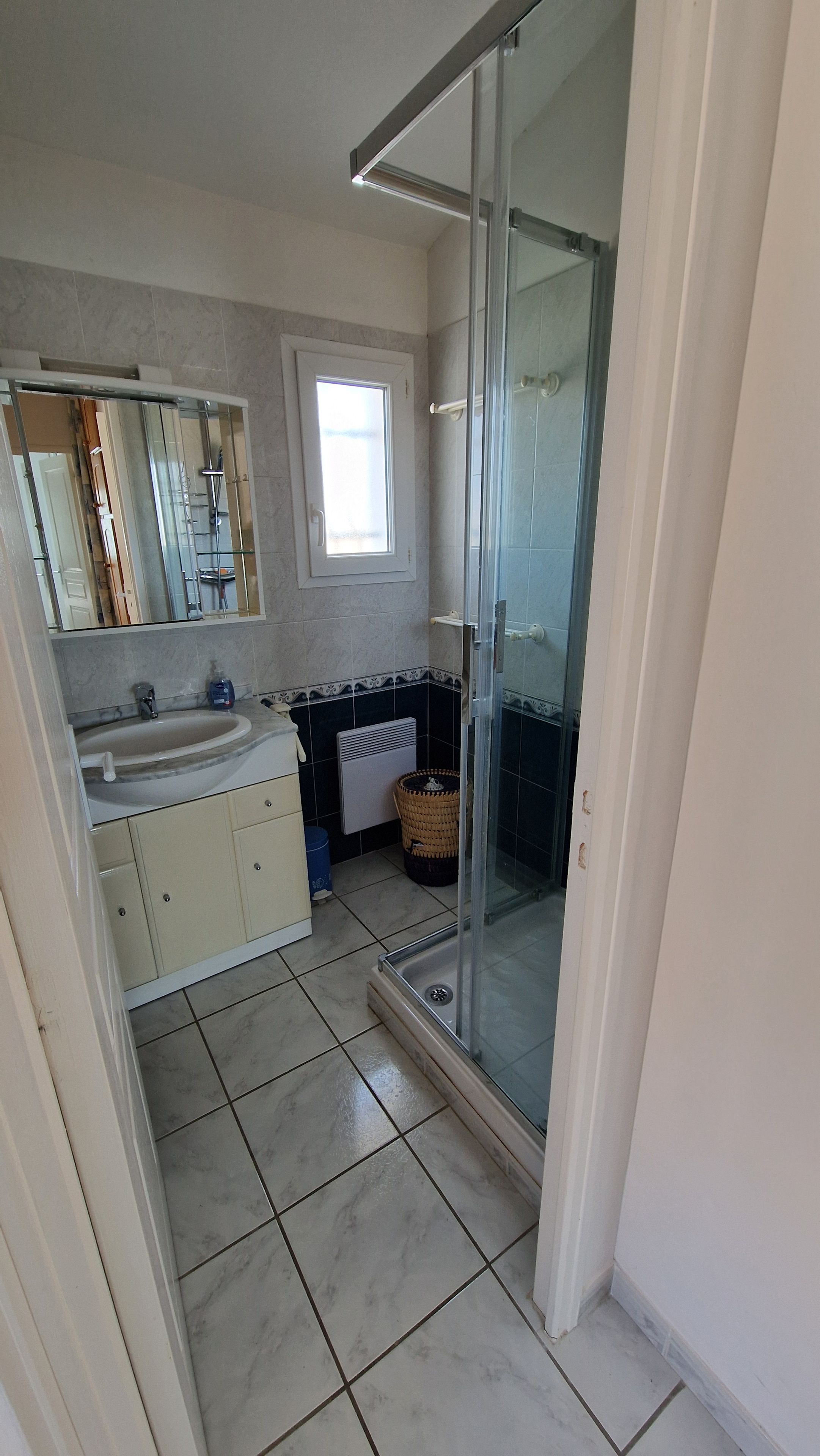Ein Badezimmer mit Duschkabine aus Glas, Waschbecken und Spiegel.