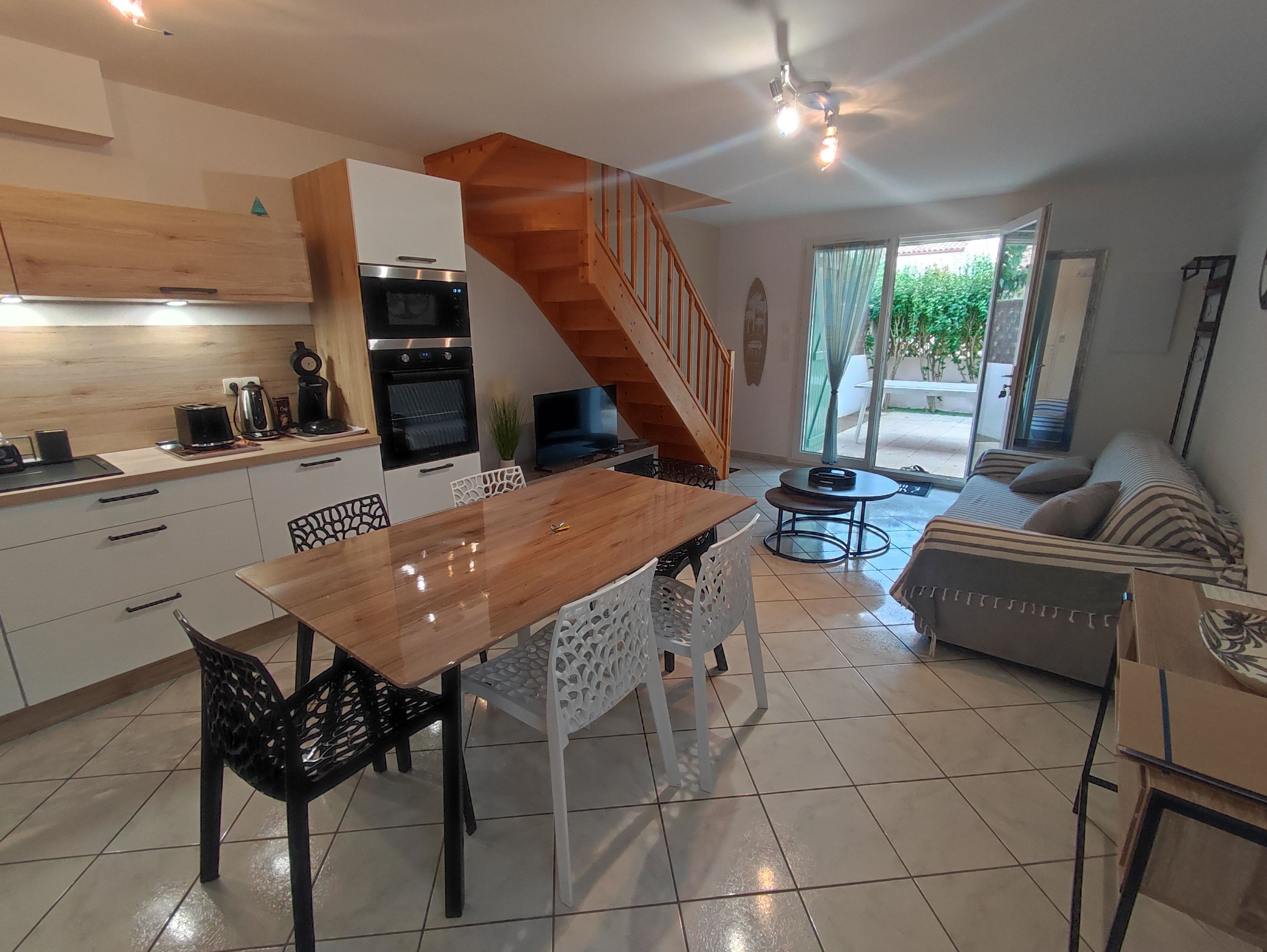 Una cocina moderna con una escalera de madera, un comedor con mesa de madera y una sala de estar con sofá.