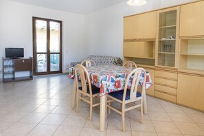Een eetgedeelte met een tafel voor vier personen, houten stoelen, een televisie op een standaard en een kast met glazen deuren.