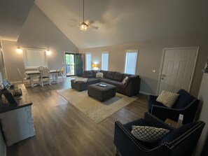 A spacious living room with a large sectional sofa, a dining area with a table and chairs, and a ceiling fan.