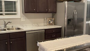 Una cocina con gabinetes de madera oscura, un refrigerador de acero inoxidable, un lavavajillas empotrado y una pequeña mesa con taburetes.