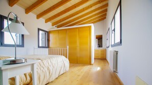 A bedroom with a wooden floor, a bed with a white headboard, a bedside table with a lamp, and a wardrobe with sliding doors. - Villa Son Paparra in the center of Mallorca. (Montuiri)