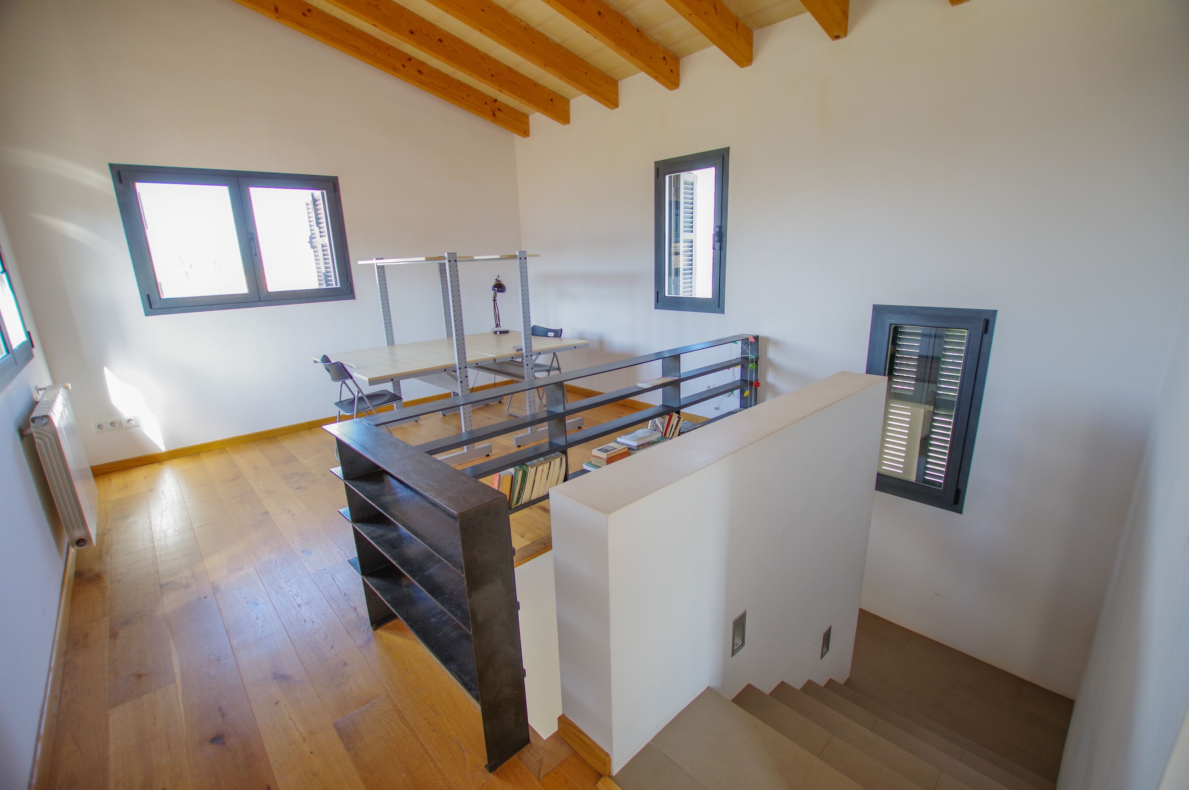 Una habitación amplia con piso de madera, una escalera y una pequeña mesa con una silla.