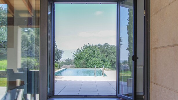 A modern room with a glass door leading to a pool area. - Villa Son Paparra in the center of Mallorca. (Montuiri)