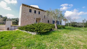 A stone building with a flat roof, a small porch, and a well-maintained lawn with white flowers. - Villa Son Paparra in the center of Mallorca. (Montuiri)
