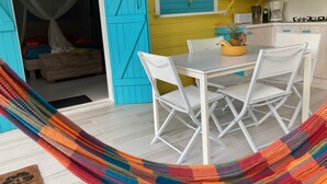 Une pièce avec une table et des chaises blanches, un hamac, un lit à baldaquin et un coin cuisine équipé d’une cuisinière et d’une machine à café.