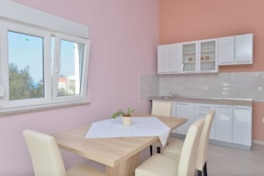 A modern kitchen with white cabinets, a dining table with chairs, and a window with blinds.