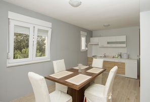 A modern kitchen with white cabinets, a wooden countertop, and a window with blinds.