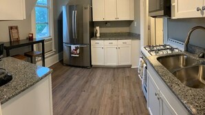A kitchen with a stainless steel refrigerator, white cabinets, granite countertops, a gas stove, and a window.