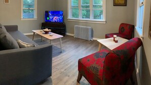 A living room with a sofa, a red armchair, a coffee table, a TV, and a radiator.