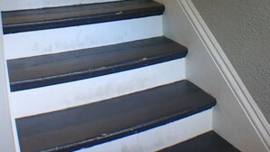 A staircase with dark steps and white trim, leading to a room with a white door and a light fixture.