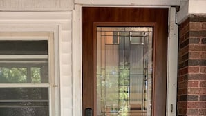 A wooden front door with a glass panel, a window with horizontal blinds, and a brick wall.