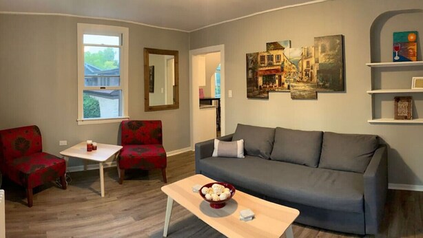 A living room with a grey sofa, red armchairs, a wooden coffee table, and a painting on the wall.