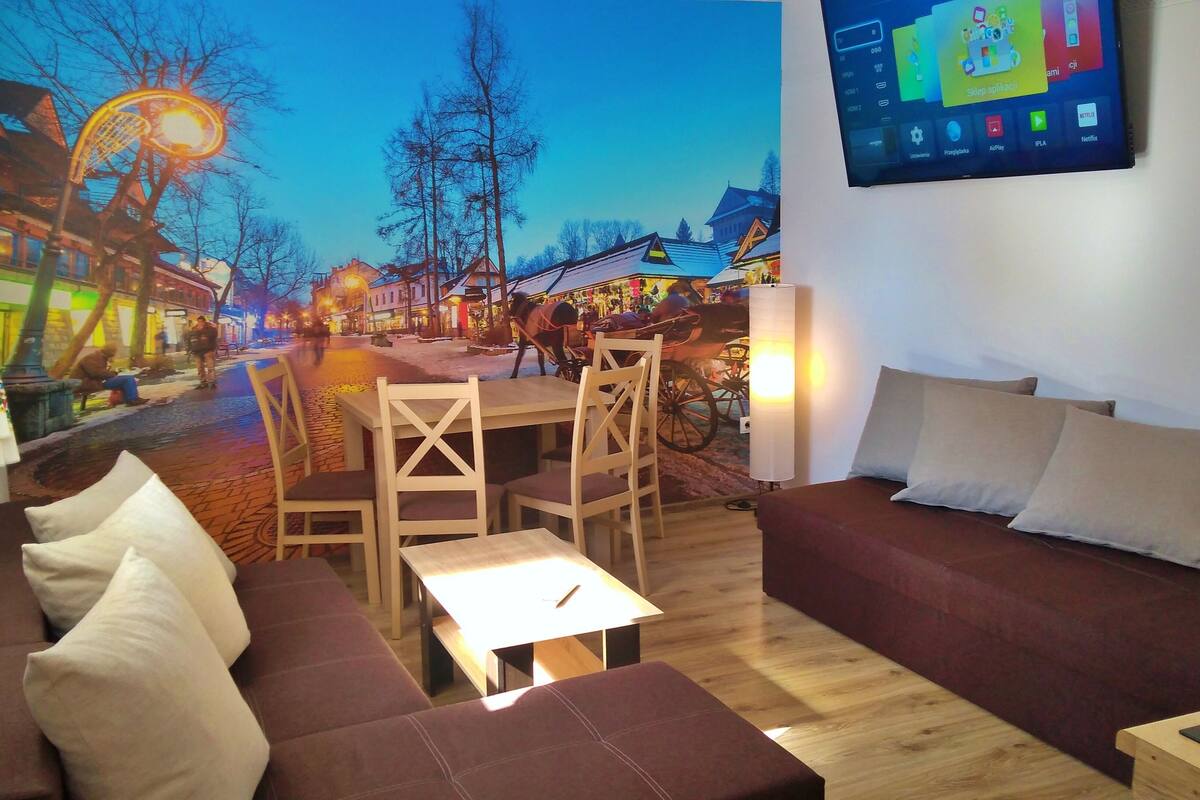 Un salon confortable avec un canapé, une petite table et un téléviseur fixé au mur.