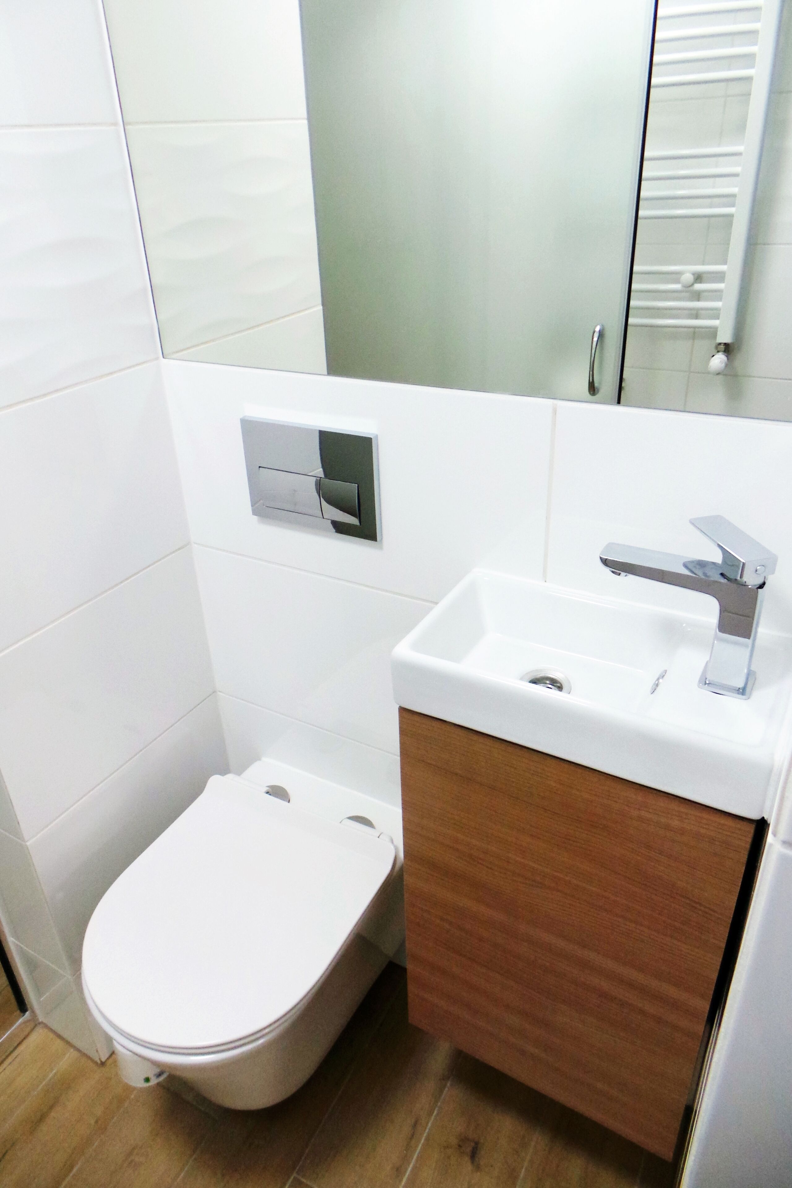 A small bathroom with a white toilet, a wooden vanity, and a mirror above the sink.