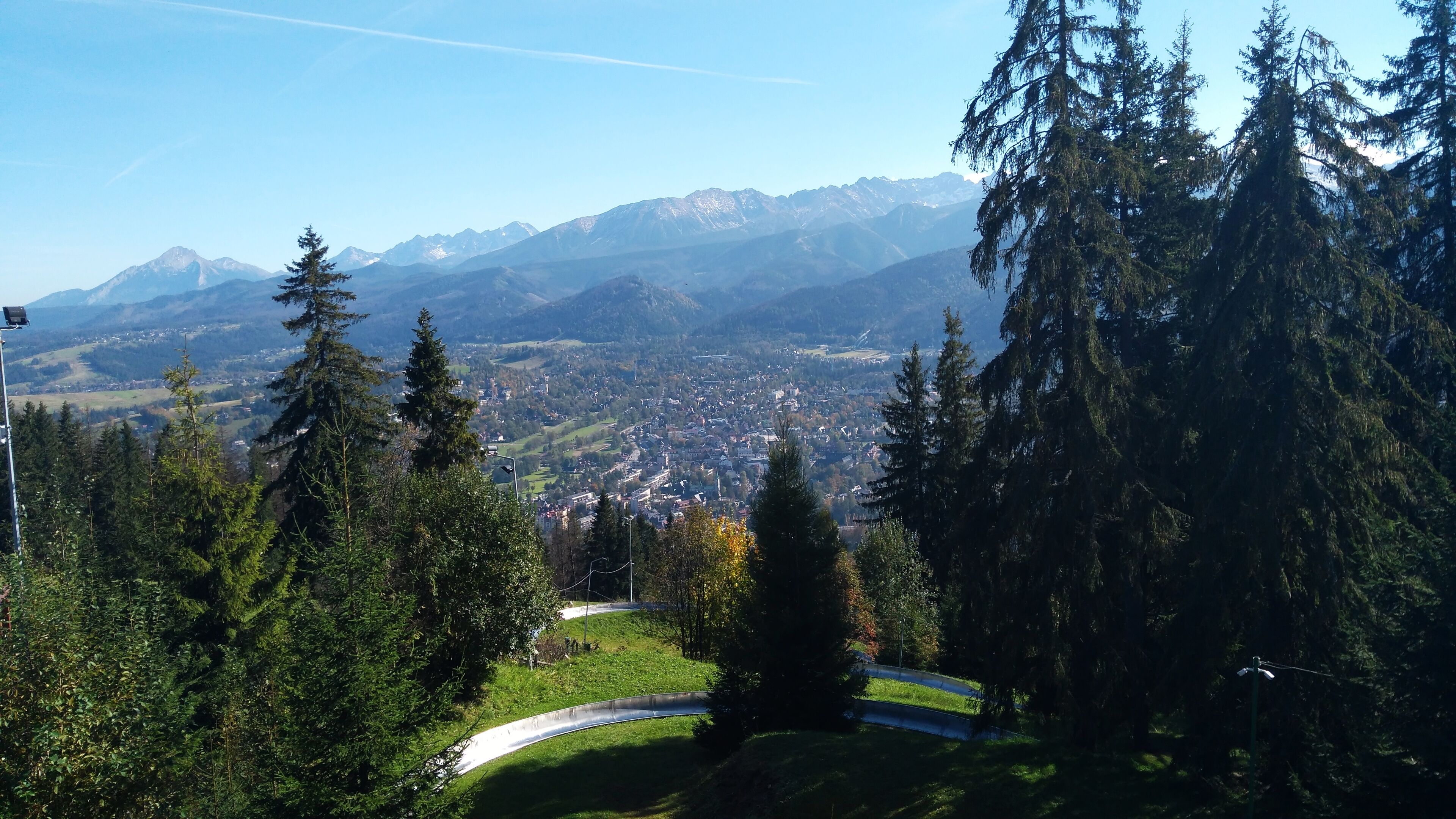 Vista panorámica de un pueblo rodeado de montañas, con un bosque denso en primer plano.