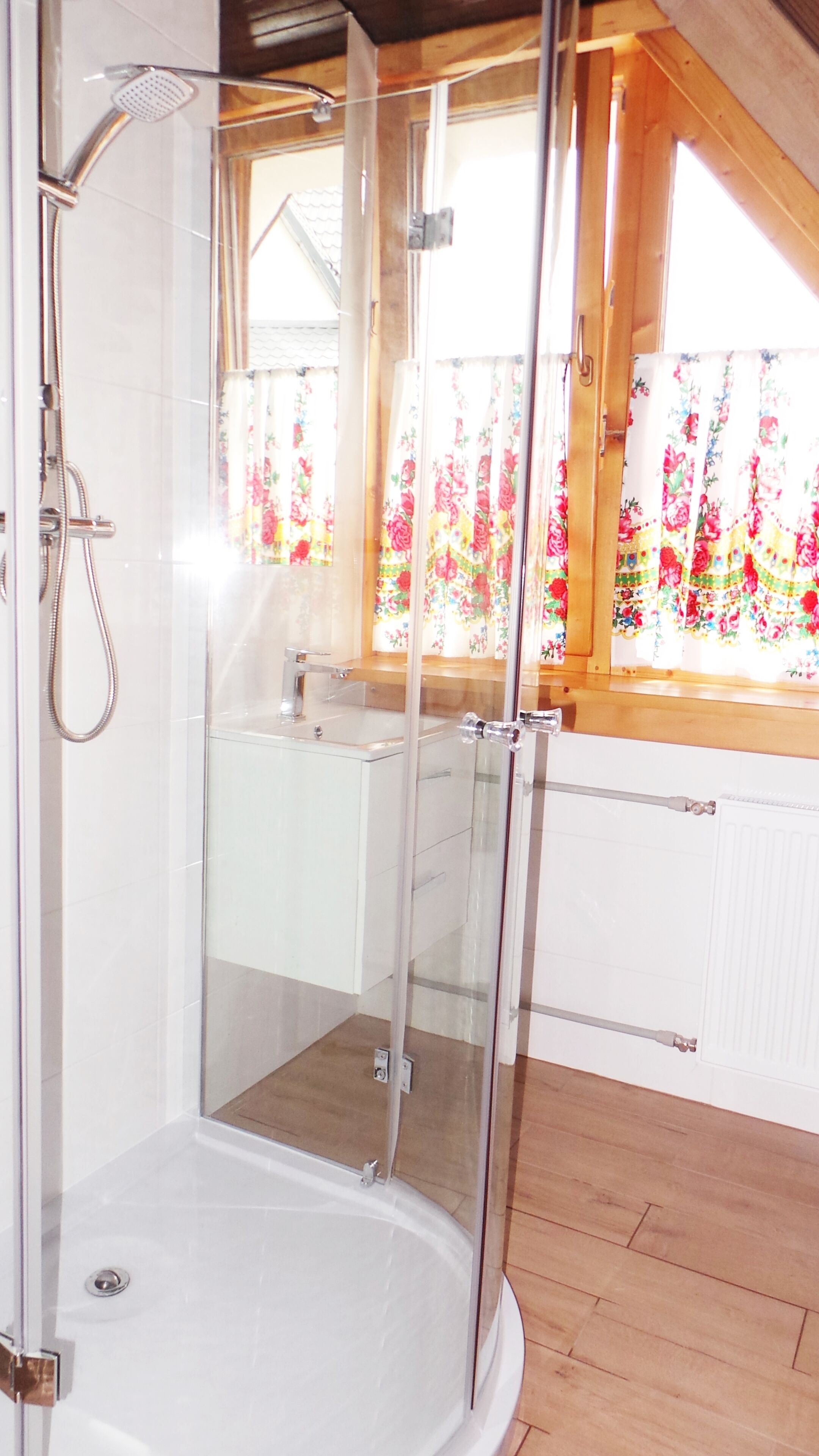 A glass-enclosed shower with a wooden ceiling and a view of a bathroom with a sink and window.
