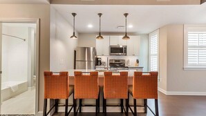 A modern kitchen with stainless steel appliances, a dining area with orange chairs, and pendant lighting. - King Street Boutique Resort (Charleston)