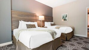 Une chambre d’hôtel avec deux lits, une tête de lit en bois, une lampe de chevet et une œuvre d’art encadrée au mur.