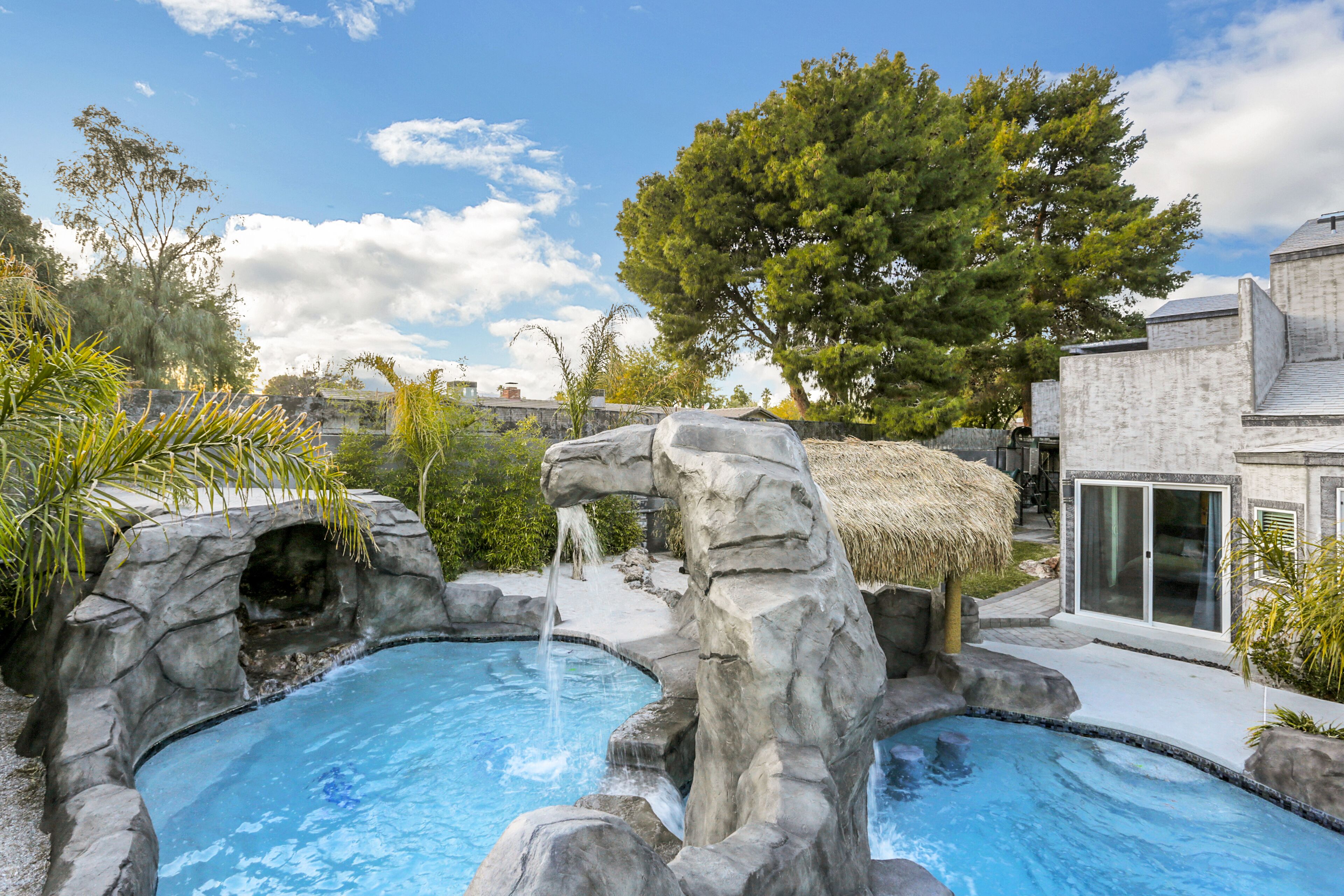 Une piscine dont le décor est constitué de rochers naturels, entourée de verdure et d’un grand arbre.