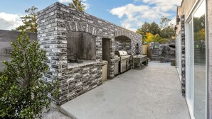 A stone-built outdoor kitchen with a grill, seating area, and a view of the surrounding landscape.