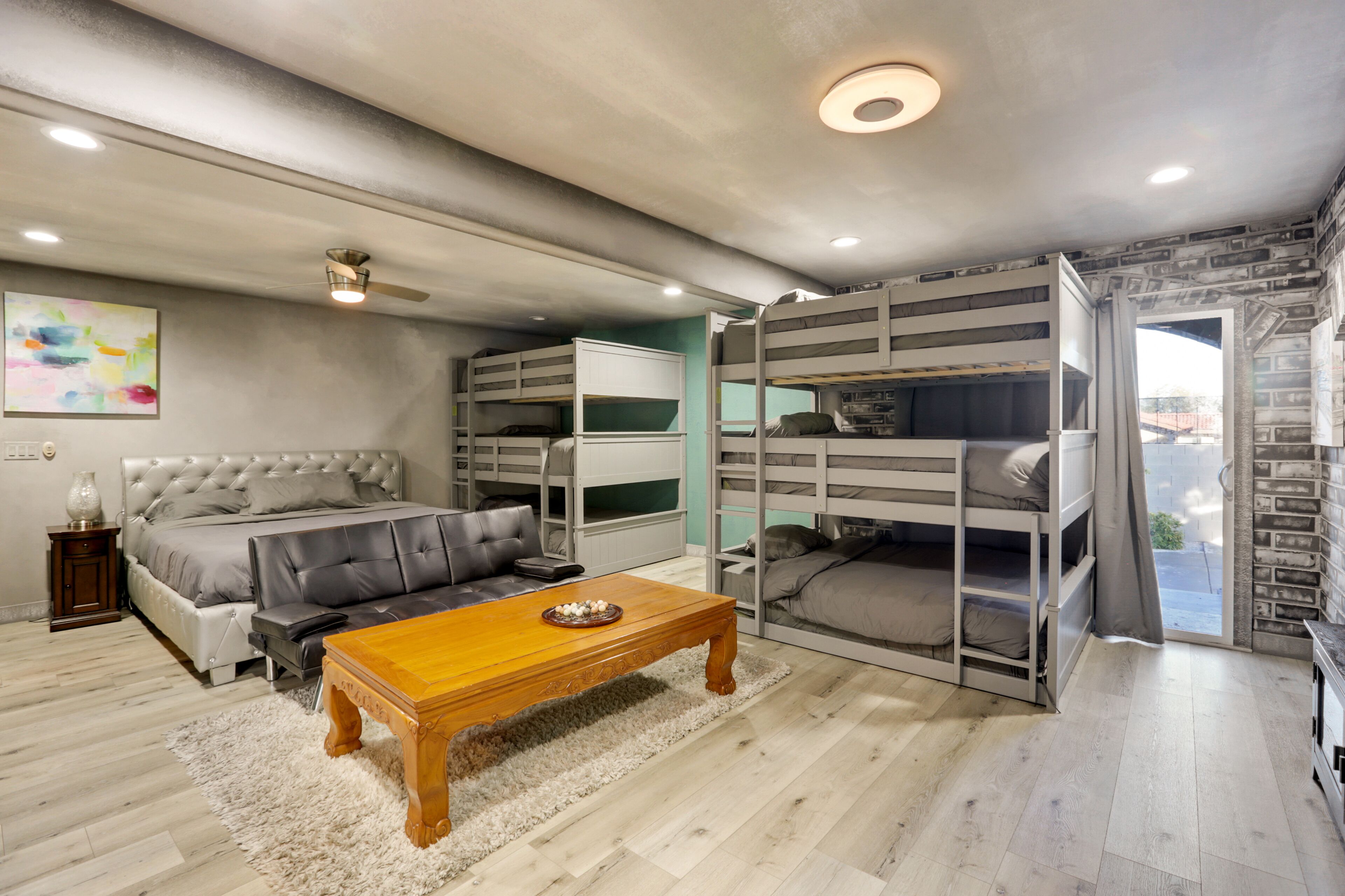 Une chambre moderne avec un grand lit, des lits superposés, une table basse en bois et un canapé gris.