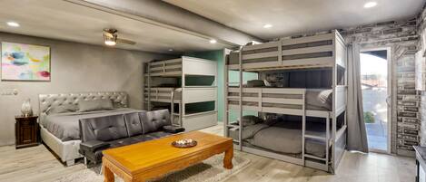 Une chambre moderne avec un grand lit, des lits superposés, une table basse en bois et un canapé gris.