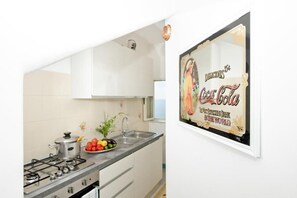 A kitchen with a gas stove, sink, and a framed Coca-Cola sign.