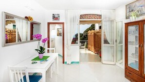 A bright room with a white table, chairs, and a potted plant. There is a large mirror on the wall and a wooden cabinet.