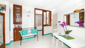 A room with a sofa, a dining table, a mirror, and a potted plant.