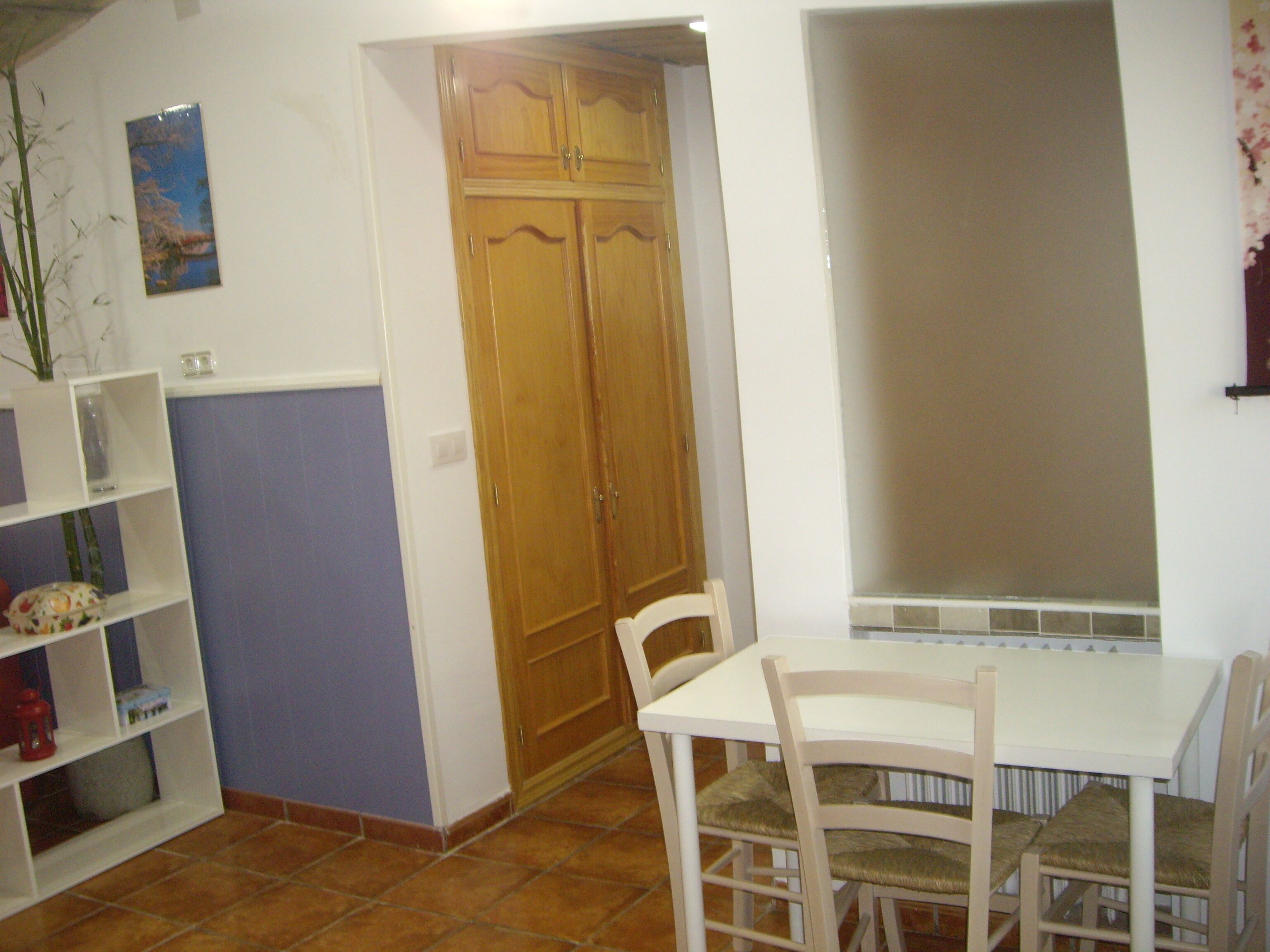 Un comedor con una mesa y sillas blancas, un armario de madera y piso de baldosas.