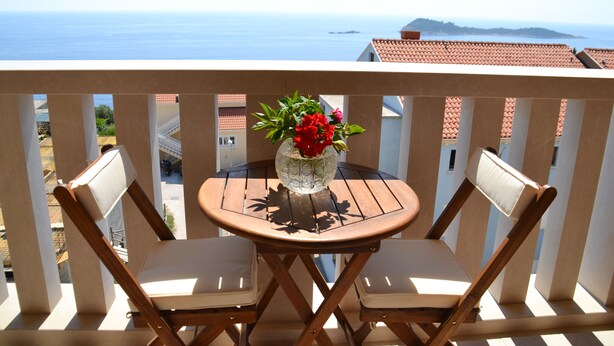 Un balcón con dos sillas y una mesa, con vistas a la costa, edificios y un cielo despejado.