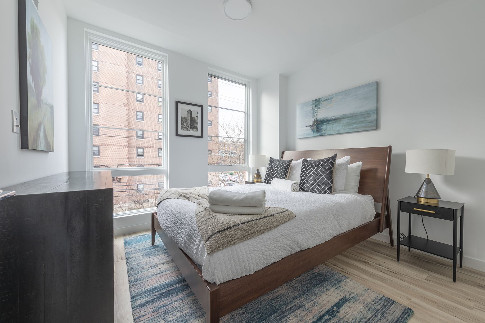 A modern bedroom with a large bed, a bedside table, a lamp, and a window with a city view.