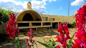 A stone oven structure with a semi-circular roof, surrounded by stepping stones and vibrant red flowers. - Domus Tilibbas - single villa, 3 bedroom suites (Olbia)