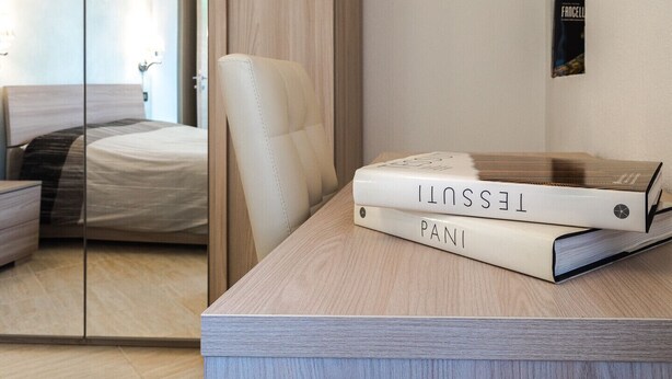 A modern bedroom with a bed, a wooden nightstand, and a desk with books. - Domus Tilibbas - single villa, 3 bedroom suites (Olbia)