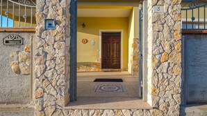 A stone entrance with a yellow wall, a wooden door, and a metal gate. - Domus Tilibbas - single villa, 3 bedroom suites (Olbia)