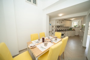 A dining area with a table set for four, a kitchen in the background, and a window providing natural light.